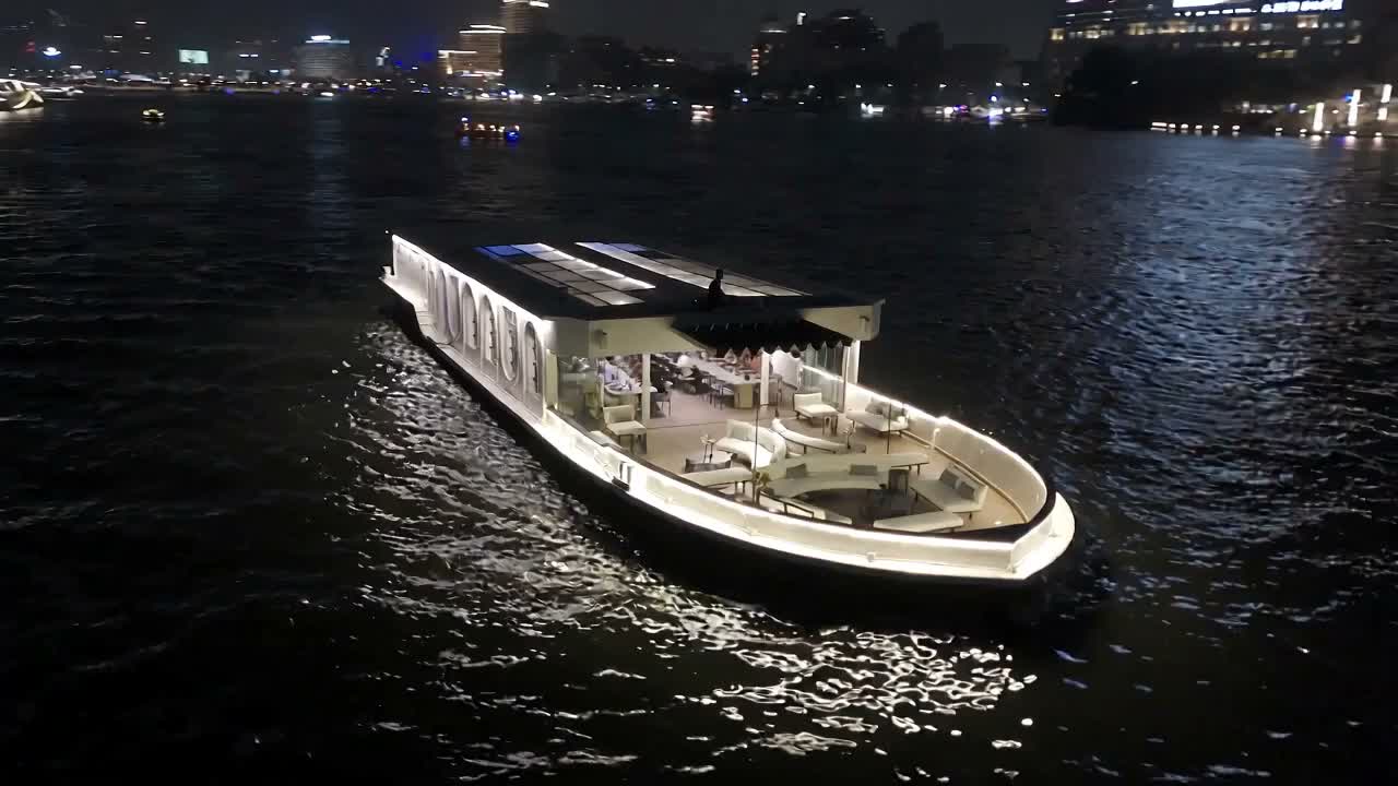 Shemu lit against the dark Nile at night, seen from the air as the camera descends toward her.